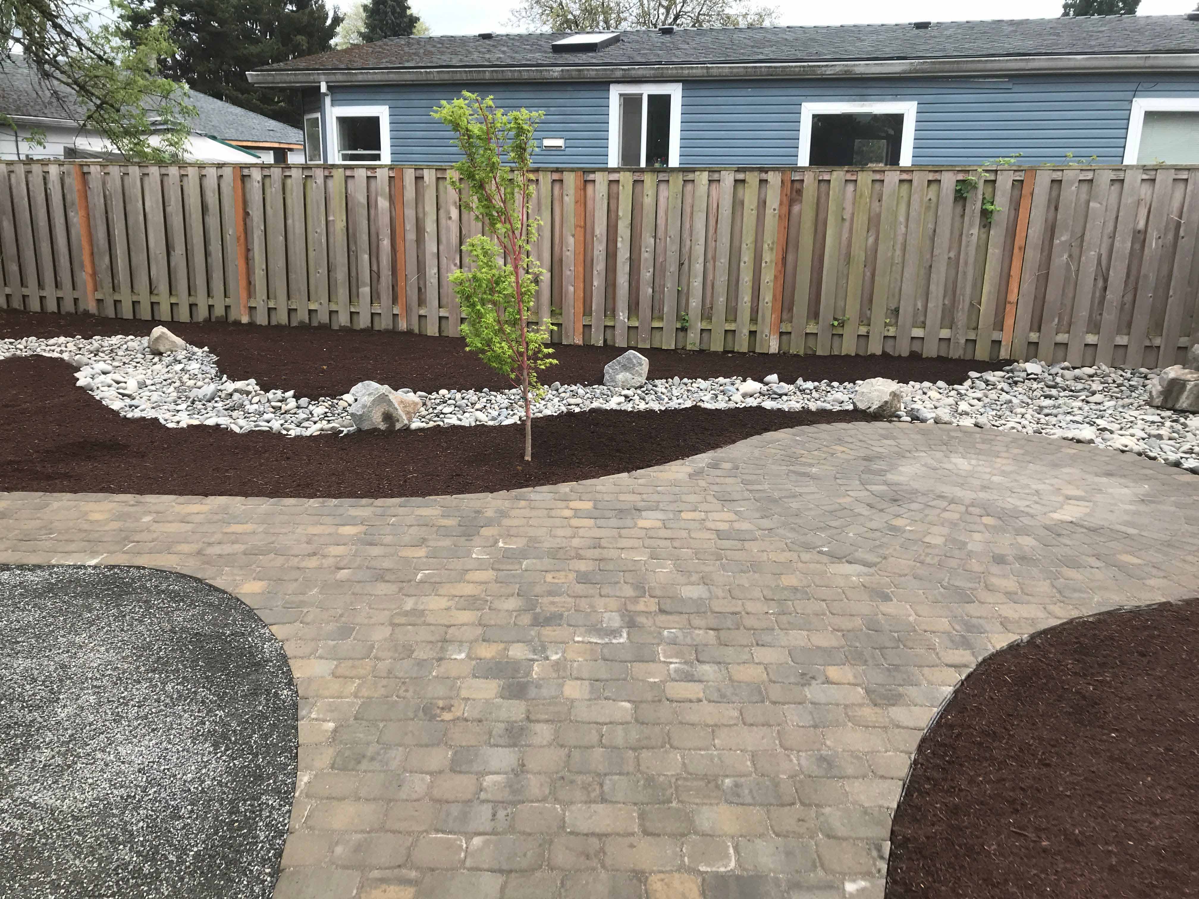 Remodeled backyard with brick path, mulched area and stone filled section