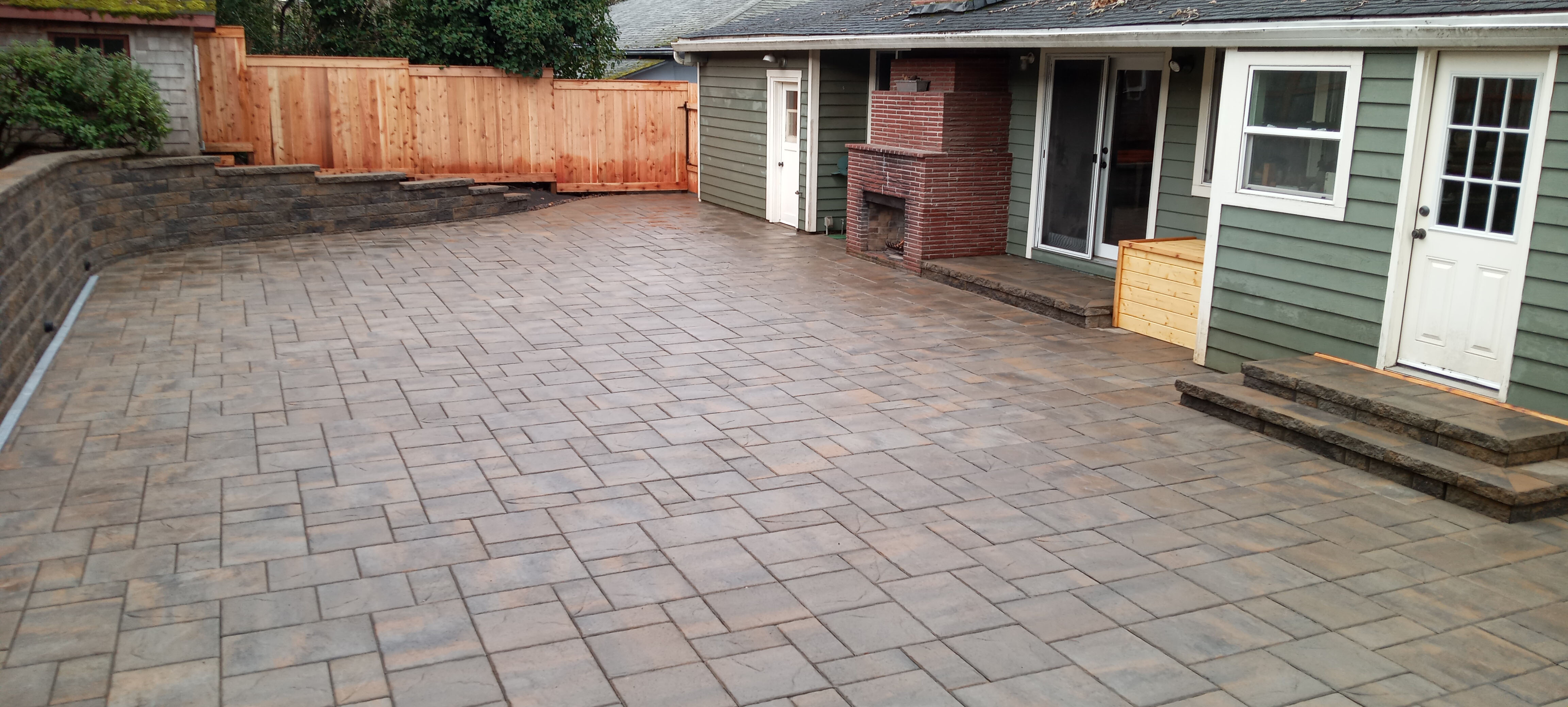 Brand new backyard patio with stone tile flooring and a curved brick retaining wall