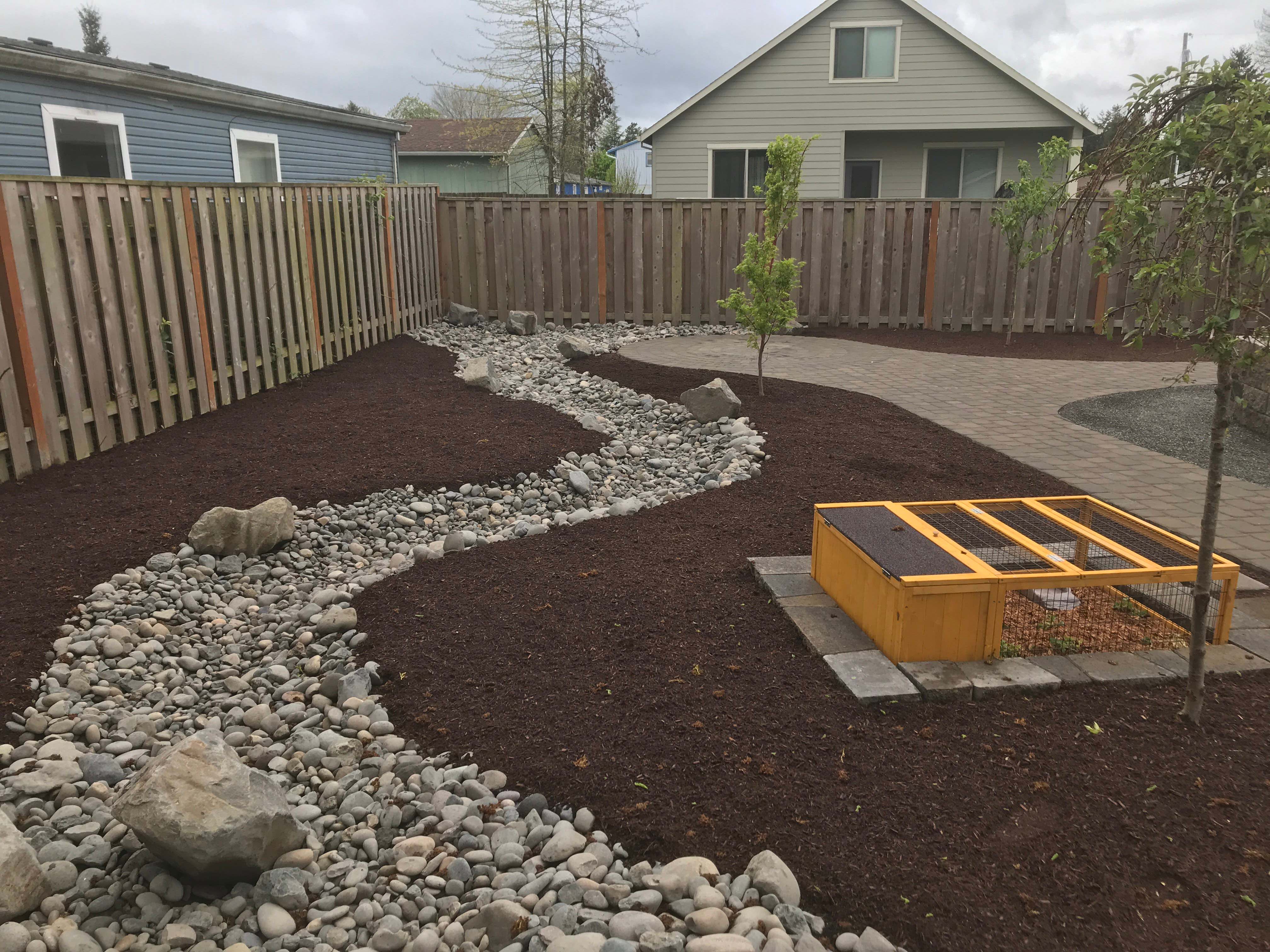 After photo of the backyard with a completely brand new layout including stone path, mulch beds, flowing stone section and newly planted trees