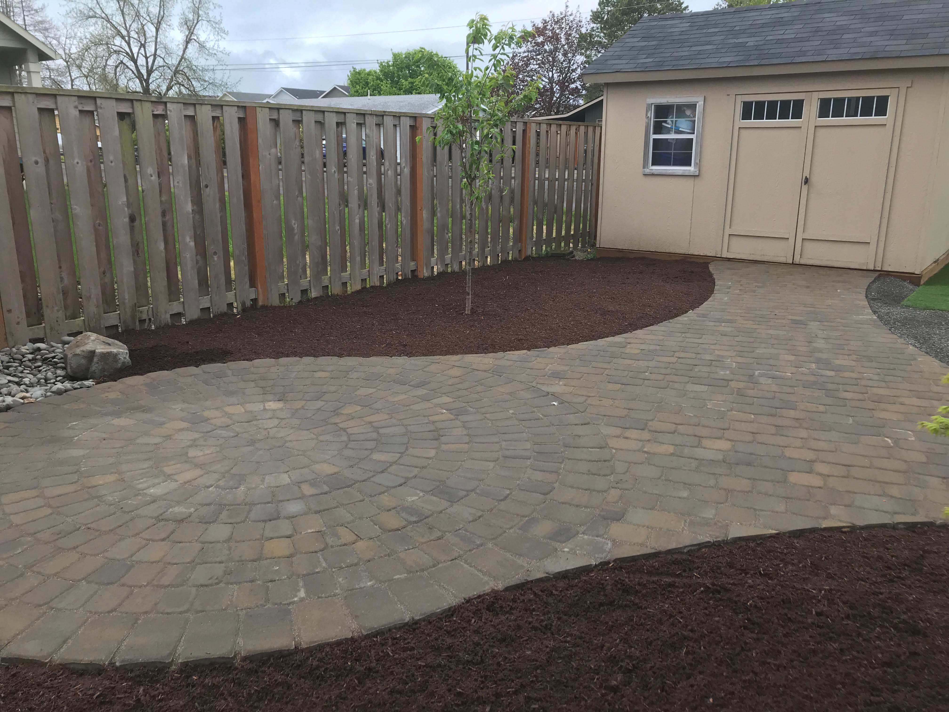 Freshly laid mulch with new trees and brick stone path leading to the backyard shed