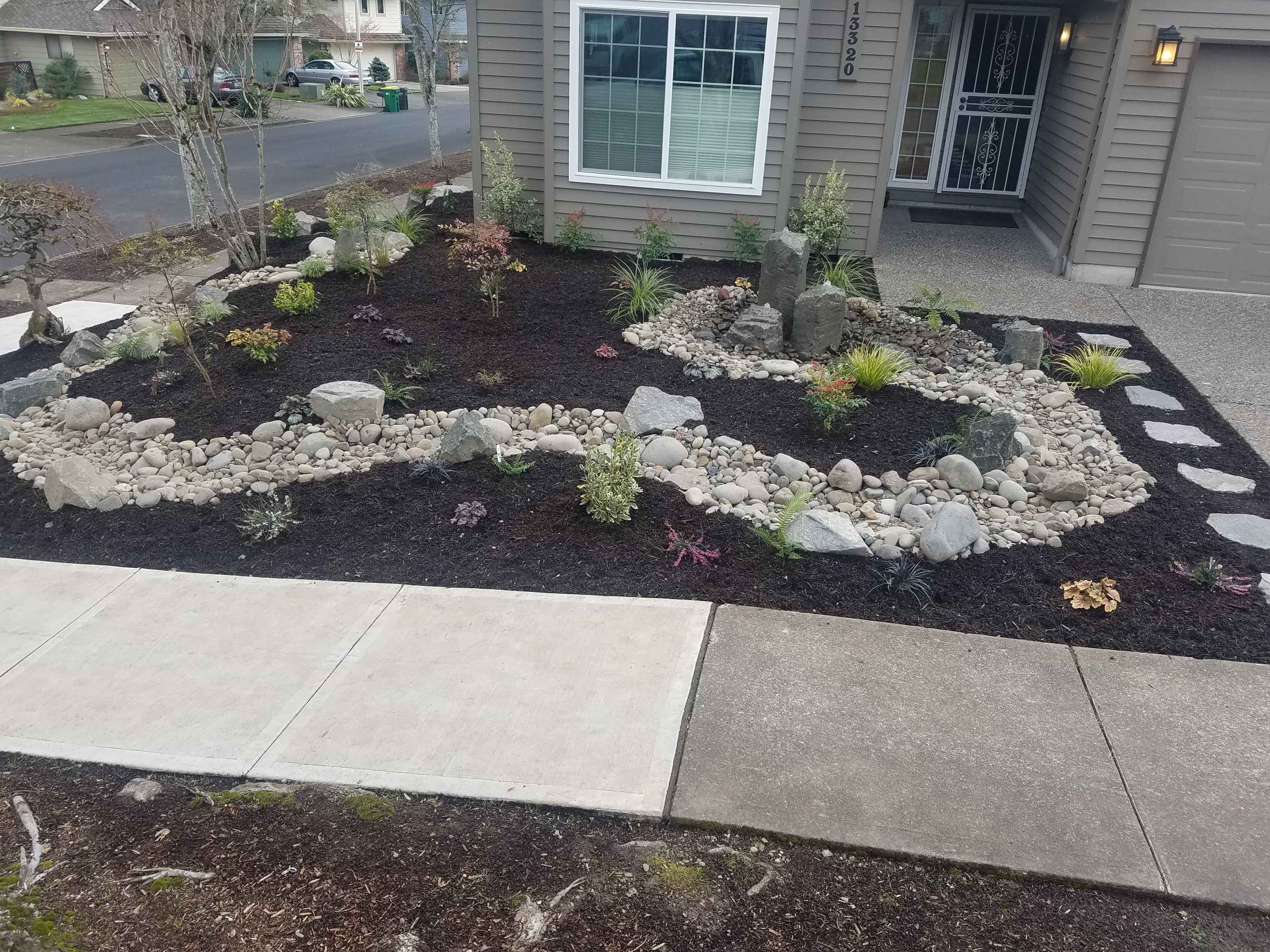 Fully remodeled backyard landscape with cement walkways, metal railings, dirt beds, gravel beds and newly planted trees with ring retaining walls