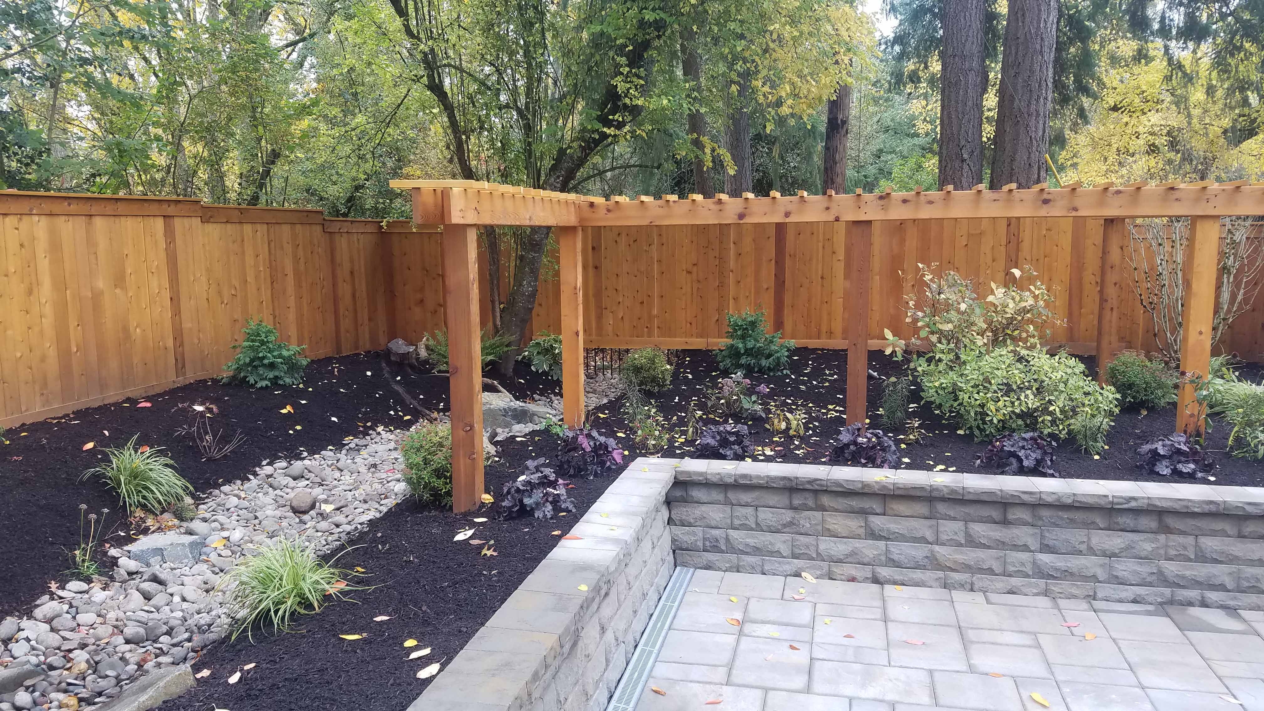 Fully remodeled backyard landscape with cement walkways, metal railings, dirt beds, gravel beds and newly planted trees with ring retaining walls