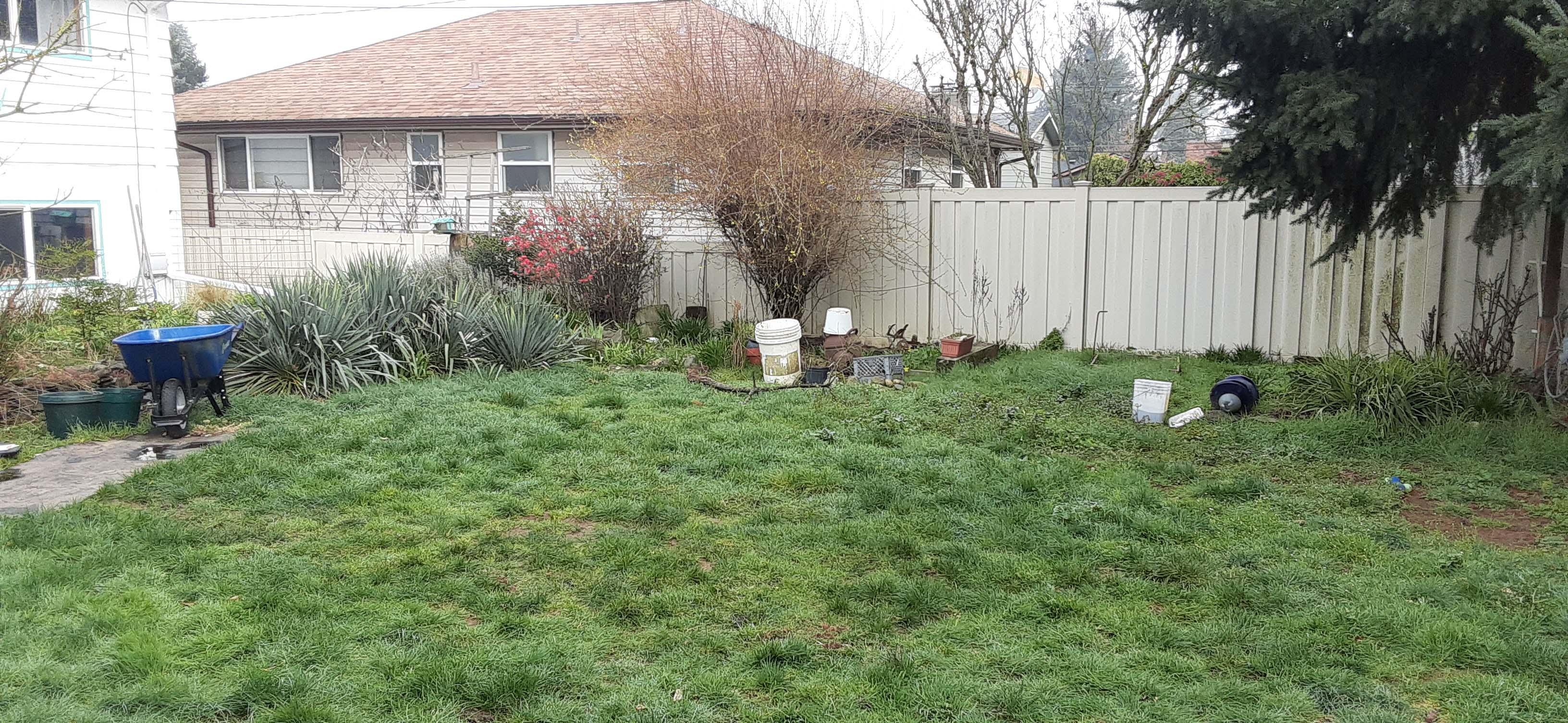Backyard with dirt path, patchy grass and decorations strewn about